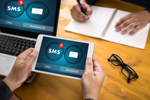 Person holding tablet showing what is business SMS notification while team works in background.