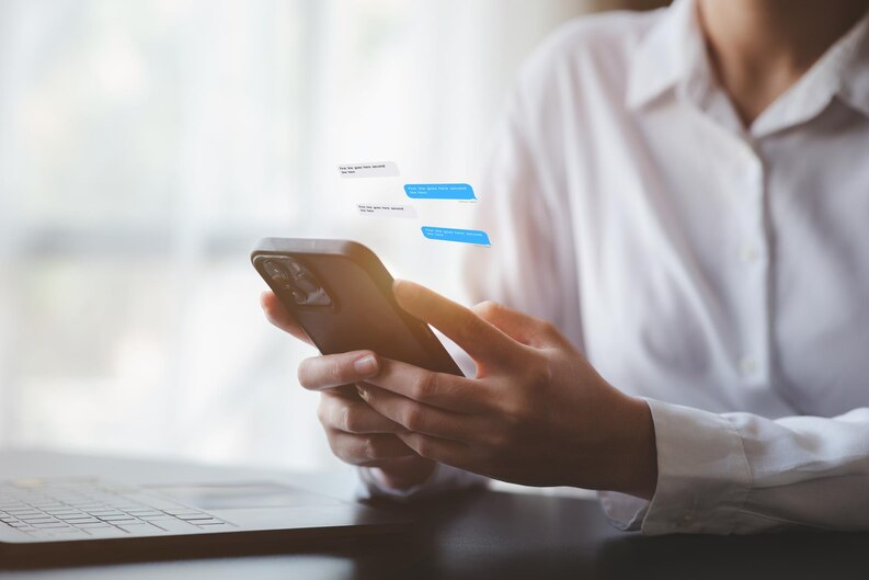 Close-up of a business person using smartphone to send automated messages via SMS messaging API, with chat bubbles appearing above the screen
